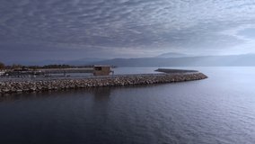 Drone footage of stone mounds surrounding piers with moored ships in Egirdir lake. Man is standing on embankment next to a marine cabin and enjoying water and mountains view. Visiting touristic places