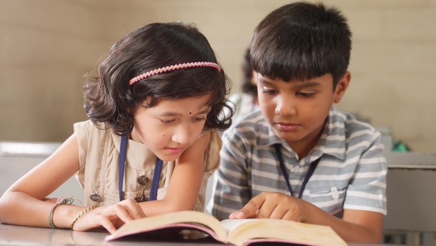 Teenage kids studying for examination while sitting on desk at classroom by sharing book - concept of education, freindship and knowledge