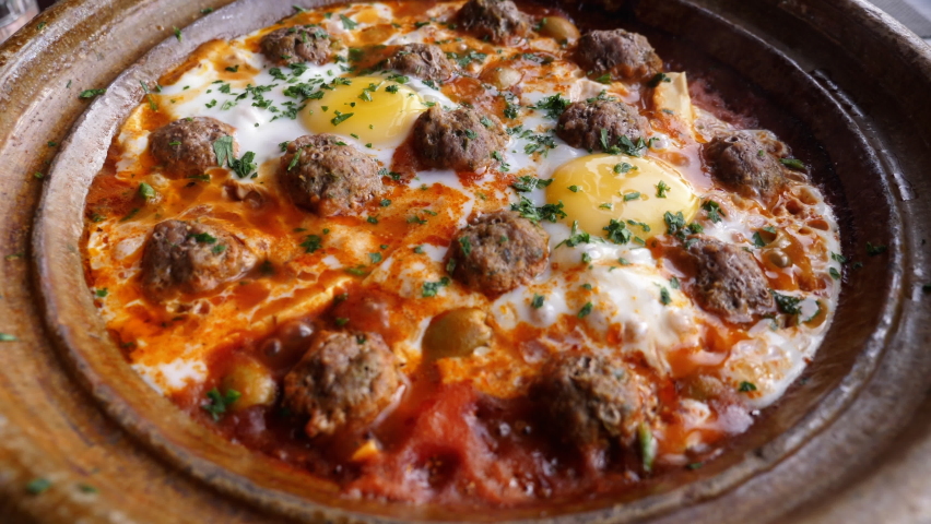 A  traditional kefta (kofta) meal served in a tajine, tagine in a Moroccan clay pot, hot, and sizzling. Traditional Moroccan slow-cooked meal with meatballs (meatloaf) and eggs. 4k. Royalty-Free Stock Footage #1092019567