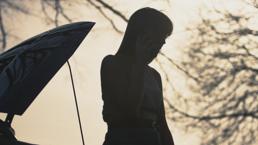 Silhouette of frustrated woman on country road standing next to broken down car with bonnet up, calling for help on mobile phone - shot in slow motion Royalty-Free Stock Footage #1092019779