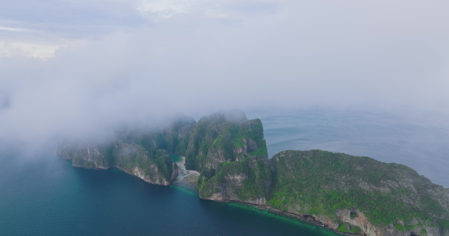 Aerial view of Phi Phi islands covered with fog tourist attraction travel landmark of Krabi, Thailand. Drone shot coming out from a thin cloud over Maya beach with beautiful blue turquoise seawater. | Shutterstock HD Video #1092021555