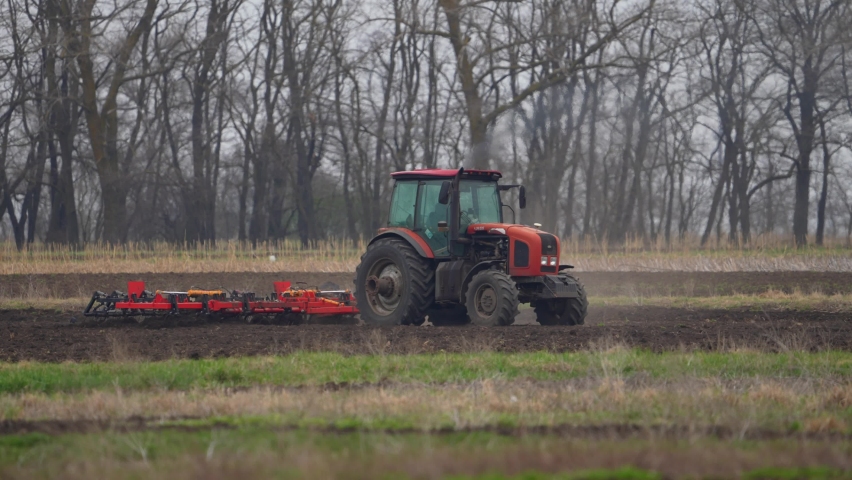 Agricultural red tractor in the field plowing, works in the field. Tractor plows the field