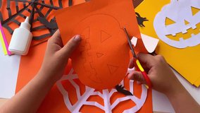 Close-up of children's hands that carves a pumpkin out of orange paper for Halloween crafts. Homemade decorations for the holiday. Hobbies, what to do with children. Selective focus. - Powered by Shutterstock - Get 15% off with code: PIKWIZARD15