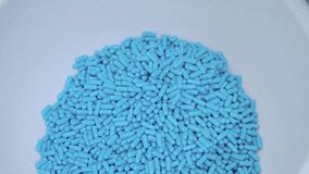 Produced blue capsules falling down to the container. close-up of pills manufactured at the drug production plant. pharmaceutical industrial concept.