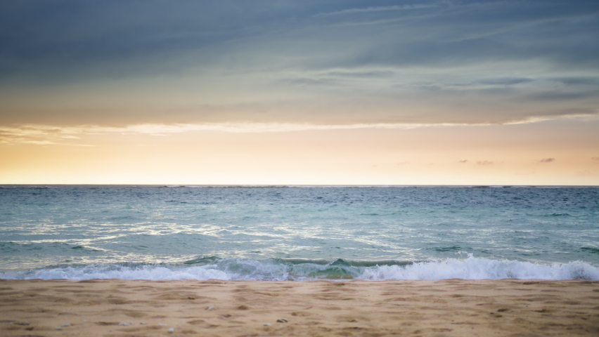 Dramatic sky with blue gray clouds above cinematic golden sunlight at clear ocean horizon. Deep blue calm ocean waves washing to the sandy beach. Summer background with copy space for promo sale offer