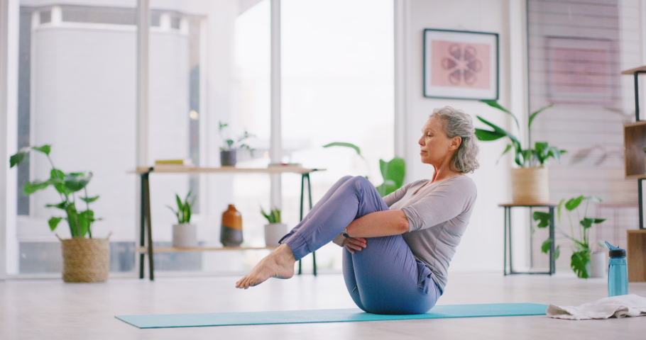 Senior woman doing yoga on a mat in a modern health facility. Active woman doing pilates, stretching her legs in a sitting position while practicing balance and meditation for a healthy lifestyle Royalty-Free Stock Footage #1092037875