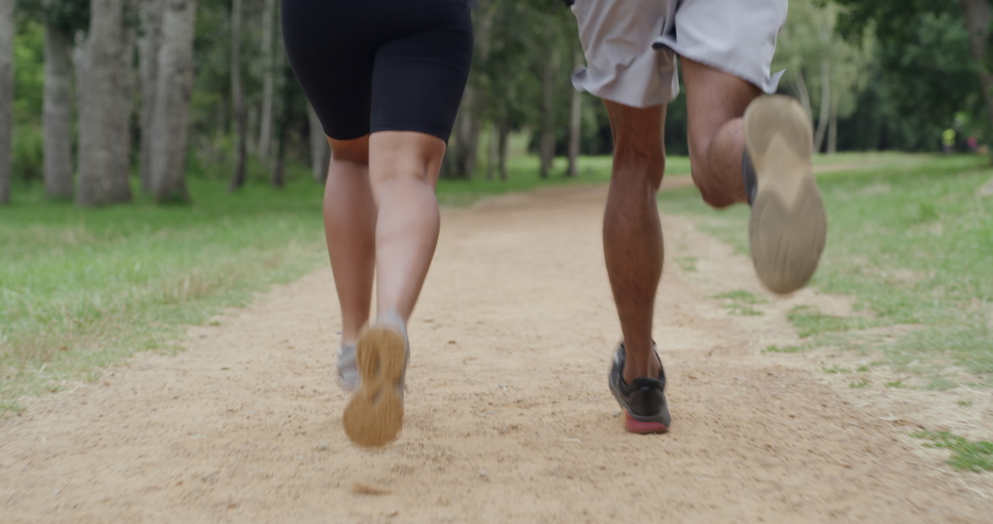 Closeup of fit couple legs running on a forest dirt road path. Active, athletic boyfriend and girlfriend bonding, training, exercising, and jogging in the woods. Man and woman in nature working out