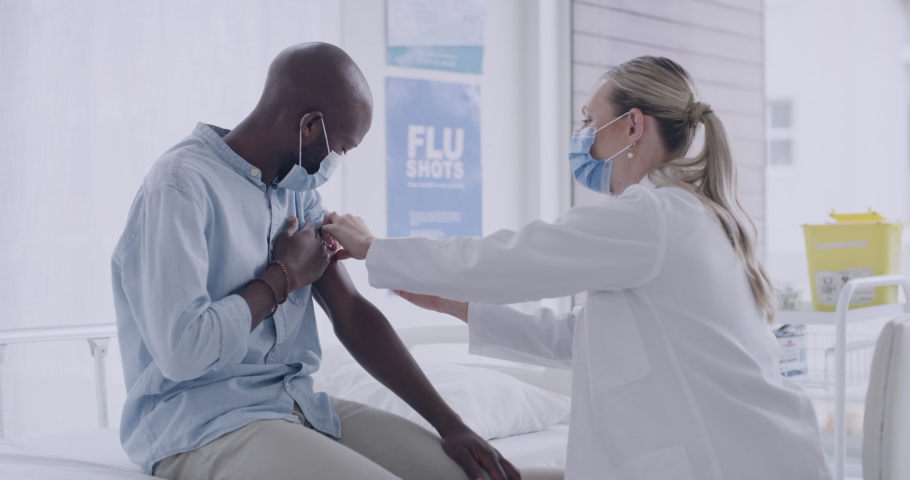 Female doctor injecting syringe with covid vaccine in arm of a male patient while wearing masks. Healthcare worker giving a patient thumbs up after receiving coronavirus immunization in a clinic