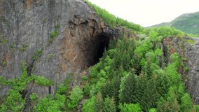 Aerial forwarding shot of a cave in a mountain hidden behind trees, Tonnes cave, Helgeland, Nordland, Norway