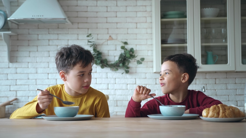 Two beautiful preschool, school kids enjoying delicious sweet chocolate cereal for breakfast while sitting at the kitchen table. Adorable children boys communicating while taking a healthy breakfast. Royalty-Free Stock Footage #1092041315