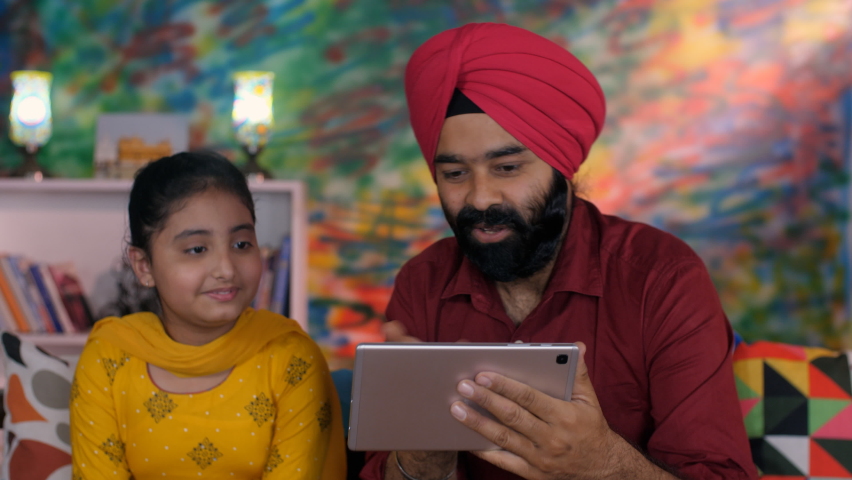 A Sikh gentleman and his little girl using a tablet - I-pad together at home - Punjabi family in India, parenting . A cute Indian girl happily watching cartoons interactive videos with her father... Royalty-Free Stock Footage #1092042089
