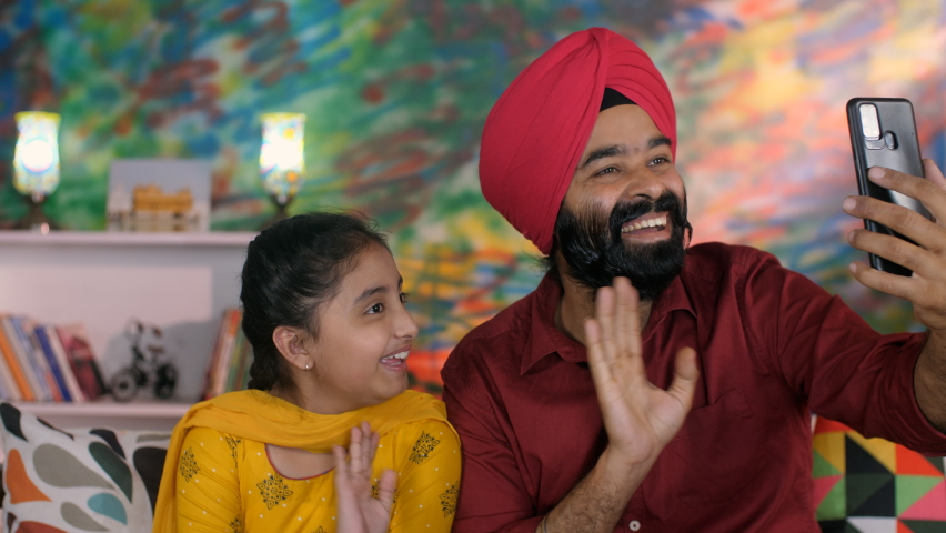 A middle-aged Punjabi gentleman and his young daughter making a video call - Punjabi family, single father. A happy Indian father-daughter duo waving their hands while chatting online - Hi gesture,... Royalty-Free Stock Footage #1092042091