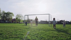 Family playing soccer on the grass. Mom and children stand at the gate and the boy kicks the ball in the stadium, slow motion video of outdoor activities together and team play.