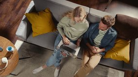 Top View Apartment: Happy Couple Using Laptop in the Stylish Living Room. Looking Up at Camera, Smile. On Couch: Girlfriend and Boyfriend use Computer for Online Shopping, e-business. Zoom Out - Powered by Shutterstock - Get 15% off with code: PIKWIZARD15