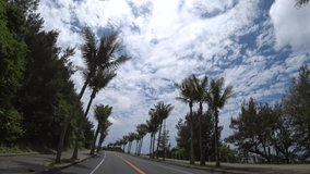 OKINAWA, JAPAN - AUGUST 2021 : Driving shot of Okinawa in daytime. Wide camera, point of view, seaside road drive. Blue sunny sky. Summer holiday, vacation and adventure journey travel concept video.