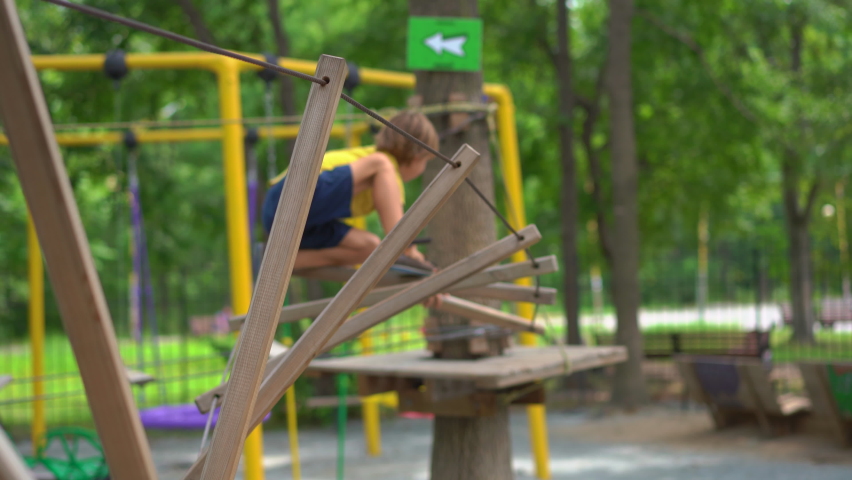 Happy child in a yellow tee-shirt, school boy enjoys activity in a climbing adventure park