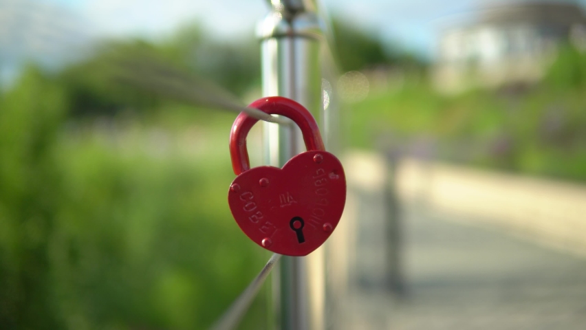 On the railing hangs a wedding lock of red in the form of a heart. A wedding tradition all over the world to hinder the lock. Monument on the wedding day. Inscription on the lock advice and love