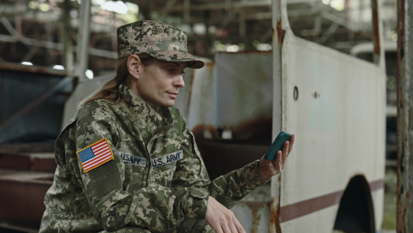 Happy caucasian US military woman smiling and waving hand during video call on modern smartphone among destroyed building. Concept of army, technology and communication. Royalty-Free Stock Footage #1092065931