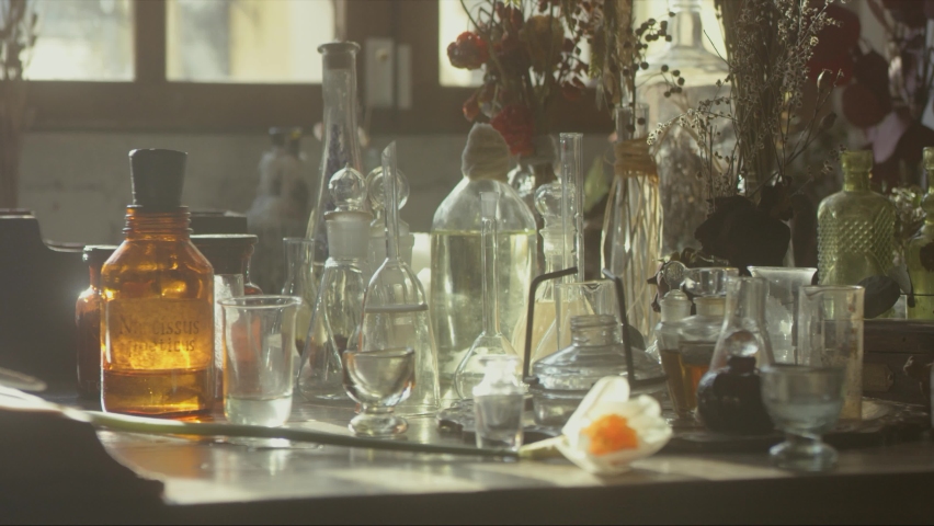 Close-up of a perfumer's workplace. Vintage cinematic concept. Sunny day in the working workshop. Lots of ingredients, a book, glass flasks on the table. Depth of field. 4K video Royalty-Free Stock Footage #1092072575
