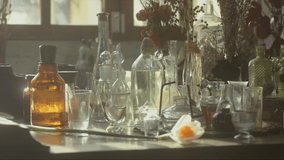 Close-up of a perfumer's workplace. Vintage cinematic concept. Sunny day in the working workshop. Lots of ingredients, a book, glass flasks on the table. Depth of field. 4K video