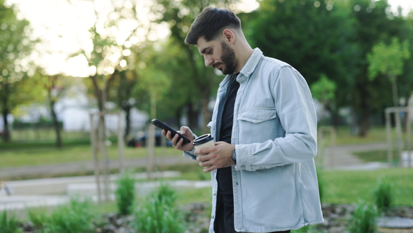 Bearded handsome arabian man having slow walk in the town, enjoying his tasty coffee. Typing messages on his smartphone and drinking hot coffee. Wearing stylish clothes. Having nice hairstyle. | Shutterstock HD Video #1092076147