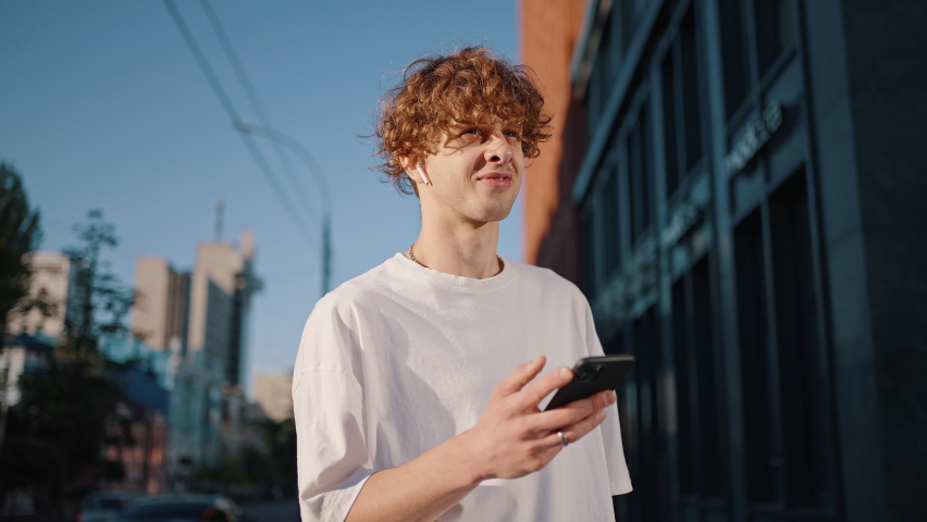 Young man dancer wearing wireless earphones turns on smartphone. Fashionable guy finds music on phone and starts dancing demonstrating strong body moves on street Royalty-Free Stock Footage #1092085829