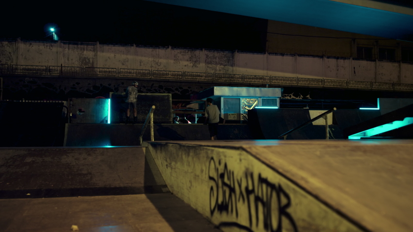Extreme friends team performing jump stunt trick on rail at night skate park. Young athletes jumping on skateboard and roller skates outside. Extreme sport youth culture action sport concept. 