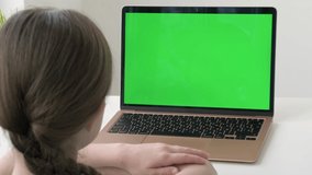 Back to school. Schoolgirl studying during online lessons at home in front of green screen laptop, back view. Chroma key, e-learning, webinar. Online distance education for children