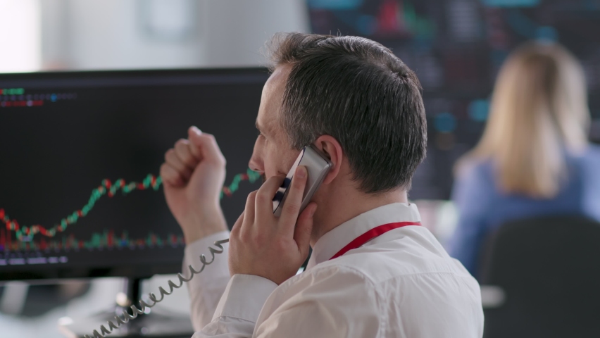 Back view of stock broker looking at computer monitor with graphs and talking on phone. Trader buy and sell shares Royalty-Free Stock Footage #1092099703