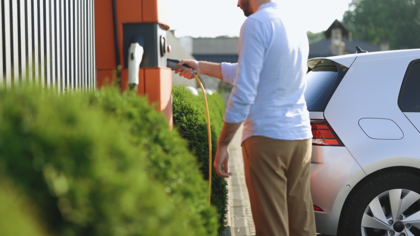 Caucasian young man charging electric car at a public charging station. Save ecology alternative energy sustainable of future. Electric vehicle charging port plugging in EV modern car. Royalty-Free Stock Footage #1092109311