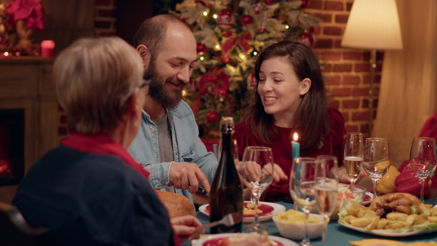Happy people talking to each other while enjoying Christmas dinner at home. Festive joyful family members celebrating winter holiday inside cozy apartment with Xmas authentic decorations. | Shutterstock HD Video #1092110007