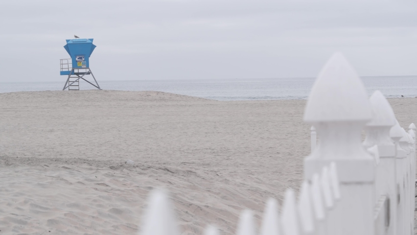 Lifeguard stand or life guard tower hut, surfing safety on California beach, USA. Rescue station, coast lifesavers wachtower or house, Coronado ocean beach, San Diego shore. White wooden picket fence.