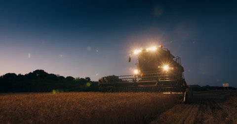 Стоковое видео: Harvester combine working at night or late evening using headlight. Farmer harvesting wheat on agricultural field at sunset. Cinematic footage of rural scenic on summertime