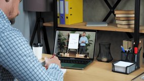 Man coach in computer screen stands near flip chart with diagrams greets talk teaches student. Businessman at home office study online business webinar course laptop, writes in notebook listen teacher