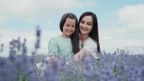 A beautiful little girl is smiling sincerely.mother and little daughter in a flowering lavender field enjoying her scent.Summer day, playing with flowers on patches.The concept of a good family. Video