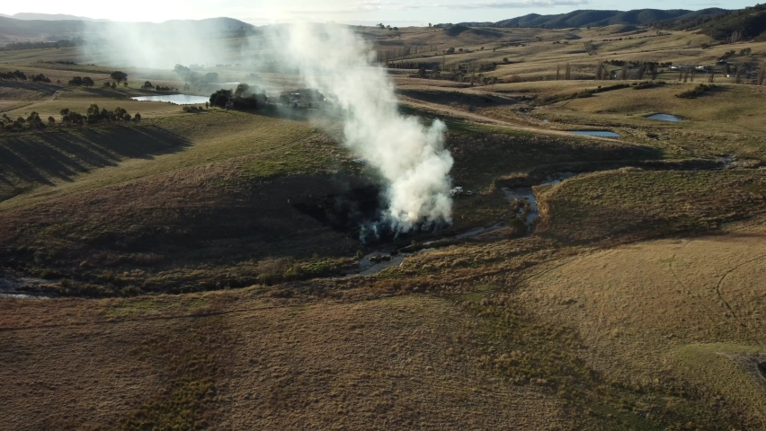 Aerial footage of small grass file in country side. Smoke blowing in the wind.