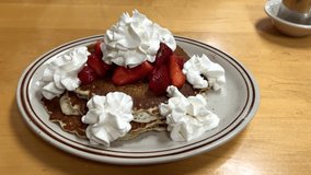4K HD video zooming in on plate of fresh homemade buttermilk pancakes with seasonal fresh strawberries covered in liberal amounts of whipped cream.
