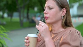 Beautiful young woman in brown dress drinking coffee in city park. 4k video footage
