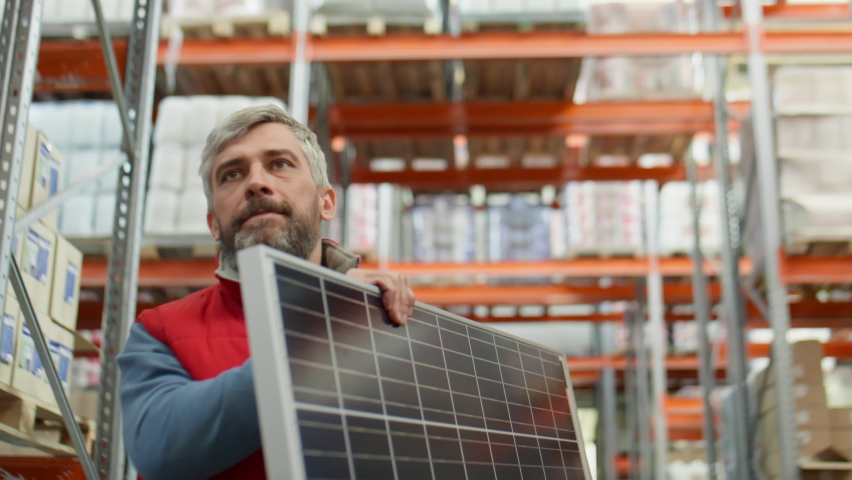 Middle aged worker with gray hair and beard walking along aisle in warehouse and carrying solar panel Royalty-Free Stock Footage #1092126877