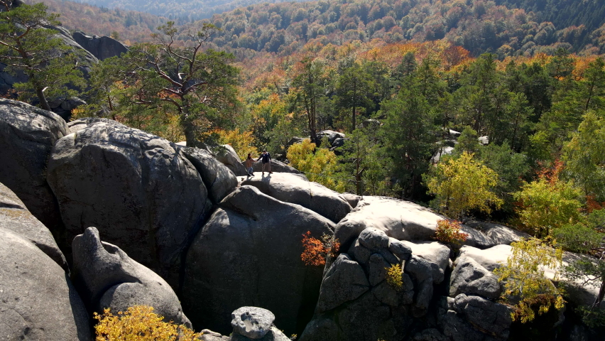 aerial orbit view of couple hikers on the top of the rock in the middle of the autumn forest carpathian mountains