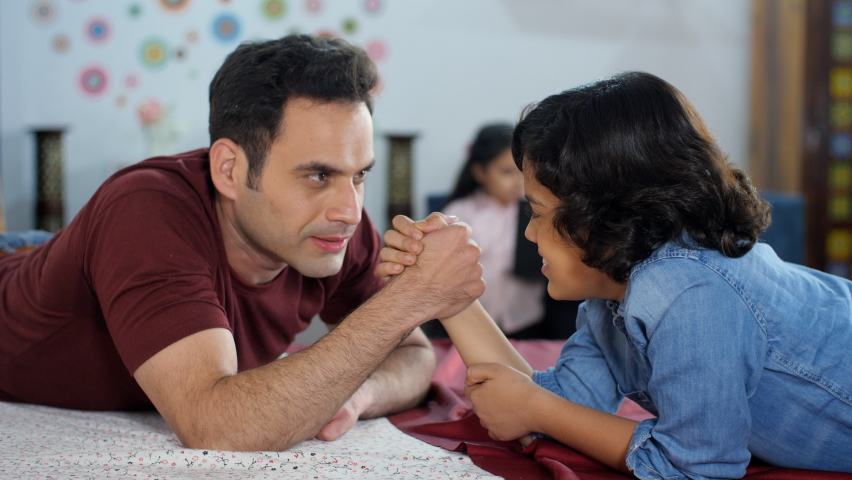 A young boy playing arm-wrestling with his father - physical strength, happy parenting, a competitive match. A happy Indian family together at home - family bonding, leisure time, an Indian househo...