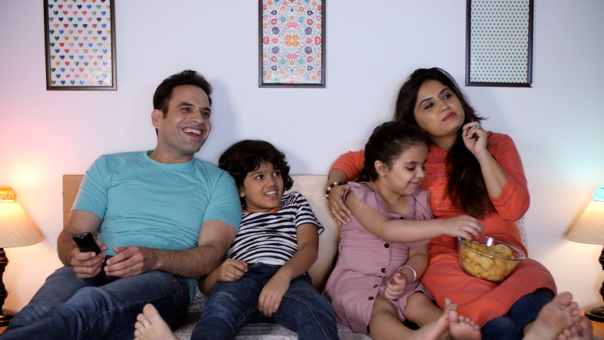 An attractive young couple and their two little kids watching television together - fun and entertainment, happy family, nuclear family. A beautiful lady and her cute daughter eating a bowl of chip... Royalty-Free Stock Footage #1092129093