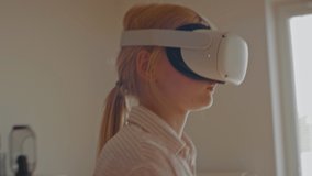 Pre teen girl wearing 360 VR headset at home, using controllers in virtual reality game. Shot with 2x anamorphic lens