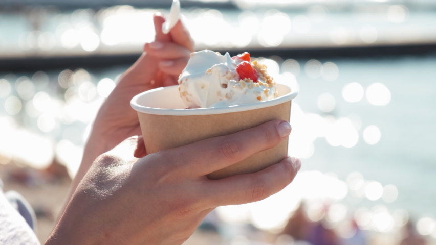 Close-up of a girl on the beach eating a newlywed. A woman eats yogurt ice cream with cherries and peanuts. a woman's hand takes ice cream with a spoon Royalty-Free Stock Footage #1092141761