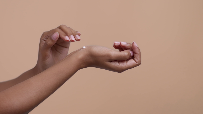 Hand care concept. Side view shot of unrecognizable black woman rubbing nourishing cream on hand skin, beige studio background, slow motion, free space Royalty-Free Stock Footage #1092143735