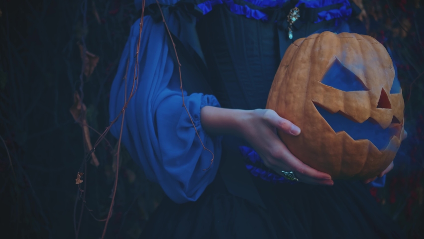 Closeup portrait attribute Halloween orange pumpkin lantern. Witch female hands hold jack o lantern. Girl cropped face. Blue misty smoke haze. Medieval pagan woman. Carnival creative vintage costume