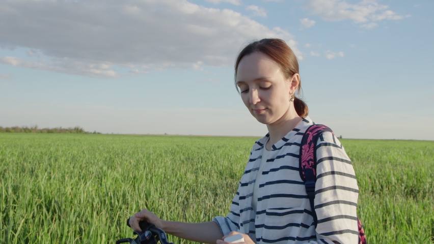4K. A young woman with a bicycle in the field puts on headphones.