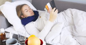 Sick young woman with bad cold, flu or coronavirus fever holding medications while consulting a doctor by video link via a smartphone. Sick woman having online medical consultation video call