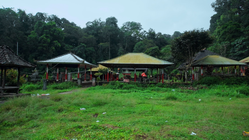 Indonesian temple standing in a field near a forest with a fence and an iron gate