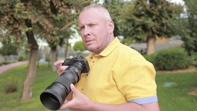 Video, an adult man makes a photo on a camera with a large lens. In the street on a sunny day in summer.